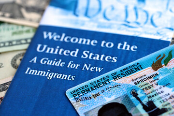 Permanent resident green card and guide for new immigrants lies on many dollar bills close up