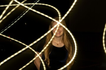 A woman stands in a dimly lit room, illuminated by bright lights behind her