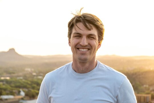 A man in a white shirt smiles for the camera atop a hill