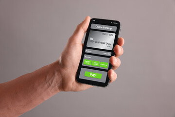 Online payment. Man holding mobile phone with open app in hand on grey background, closeup