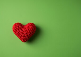 A lovely red knitted woolen heart sits centered on a vibrant plain green fabric background, symbolizing warmth and handmade care ,red ,february ,craft