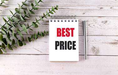 Spiral notepad with words best price and silver pen on white wooden table with green leaves