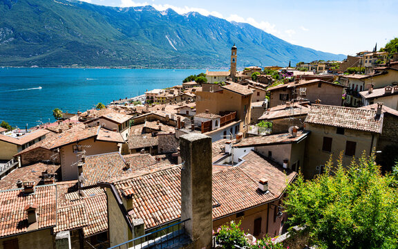 Panoramic view of Limone sul Garda, Italy, with terracotta rooftops overlooking the deep blue waters of Lake Garda and the majestic Monte Baldo mountain range under a clear summer sky.