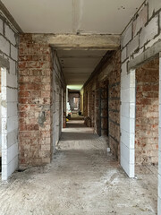 Unfinished industrial hallway with exposed concrete walls, red brick arches, bare beams, and dusty concrete floor, showcasing raw construction aesthetics