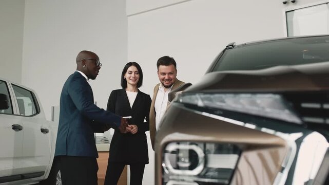 A man and woman consult with an African car dealer in a modern showroom about choosing a new vehicle. Concept assisting in car selection. - Powered by Adobe