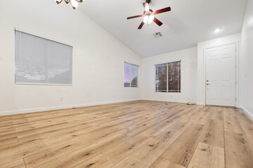 An empty living room with hardwood floors and an overhead fan
