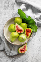 Sweet green figs in a plate with leaves and napkin on a gray concrete background.