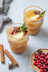 Two glasses of hot apple cider with cinnamon, anise, brown sugar and rosemary on a light background