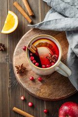 A mulled wine in a mug with cinnamon, berries and fruits on a dark wooden background with napkin.