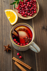 A mulled wine in a mug with cinnamon, berries and fruits on a dark wooden background.