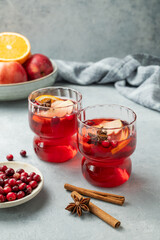 A cranberry drink in a two glasses on a light background with cinnamon, berries and fruits.