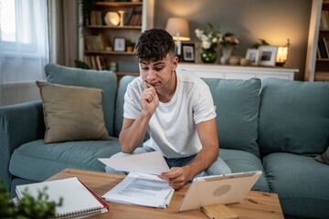 Fototapeta premium Young man feeling financial stress studying bills at home