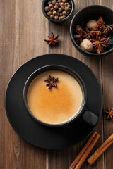 Traditional Indian masala chai tea with milk and spices in a black cup on a dark wooden background