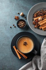 Traditional Indian masala chai tea with milk and spices in a black cup on a dark background with napkin.