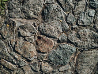 The masonry wall is made of large natural dark granite blocks. Stone background.