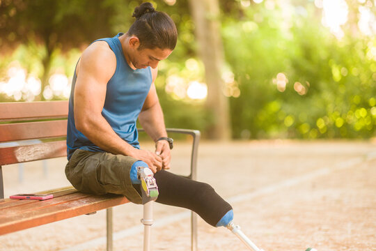 Venezuelan Middle-aged man athlete adjusting prosthetic legs on park bench - Powered by Adobe