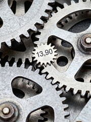 A detailed close-up of intricate metallic gears intermeshing, with one cog prominently displaying the number "13,90".