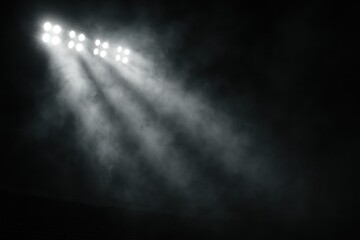 Blazing stadium floodlights slicing through swirling smoke above dark textured field