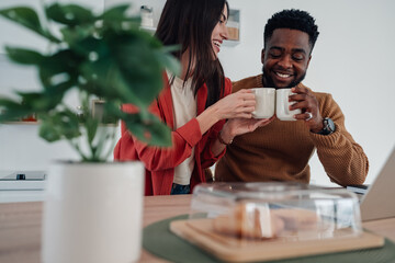 Diverse couple smiling, drinking coffee in kitchen