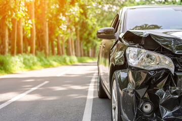 Fototapeta premium Front End of a Black Car Severely Damaged in an Accident, Stopped on a Roadside with Sunlight Filtering Through Trees. Car insurance claims, auto repair services, road safety, or legal concepts.