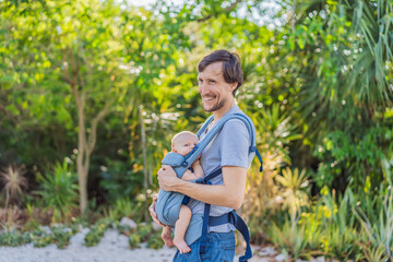 Young father walks in nature with his baby son nestled close in a parent-facing ergonomic baby carrier. Bonding, warmth, and modern parenting concept in a peaceful outdoor setting