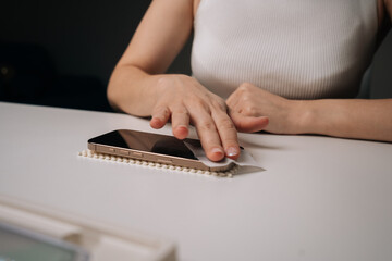 Cropped shot of woman cleaning smartphone screen with disinfectant wipe, preparing surface for installation of new glass screen protector, ensuring clean and bubble-free application.