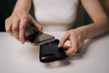 Elegant woman inserting gold smartphone into slim black case, sitting at minimalist white surface, highlighting contemporary tech lifestyle. Concept of mobile phone maintenance and service.