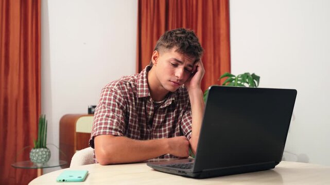A young man shows signs of frustration and stress while working on a laptop, with a thoughtful expression as he grapples with a challenging situation, highlighting the challenges of remote work.