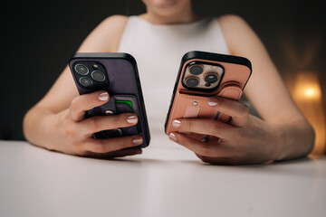 Woman holding two new smartphones with card holder cases, comparing colors and features while deciding on best option for needs. Modern technology meets style in hands