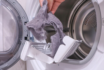 close up female hand taking lint out from dirty air filter of dryer machine after drying. cleaning Dirty filter. hair, wool from filter in hand. Front Load Tumble Laundry electric Dryer Machine. 
