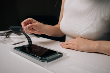 Fototapeta premium Cropped shot of woman installing screen protector on smartphone using specialized machine, ensuring perfect alignment and protection against scratches. Concept of mobile phone maintenance