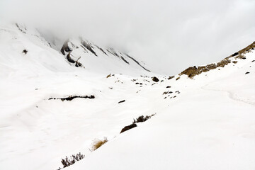 Trekkers navigate a snow-covered trail in the Himalayas, en route to Annapurna Base Camp in Nepal. Mountains are shrouded in mist on a cold, overcast day.