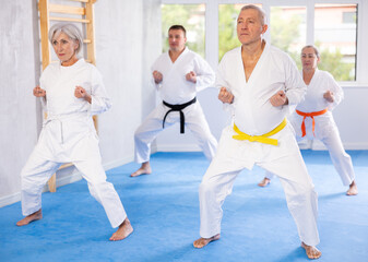 Active mature man wearing kimono training karate techniques in group during workout session