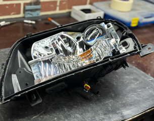 Car headlight in repair closeup. The car mechanic installs the lens in the headlight housing. The concept of a car service.Installation of LED lenses in the headlight. LED lens. Restoration of optics.