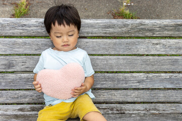 ハートのクッションを持ってベンチに座る男の子（2歳、日本人）