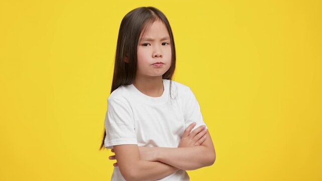 A young Asian child stands confidently with arms crossed, showcasing a serious expression.