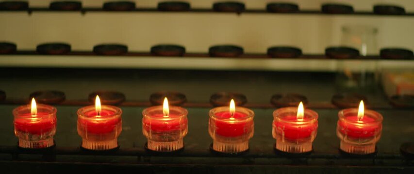 Row of small red votive candles burning in a church prayer area close-up