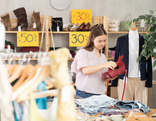 Teenage girl stands in a store and chooses clothes and accessories at discounts, she is looking at...