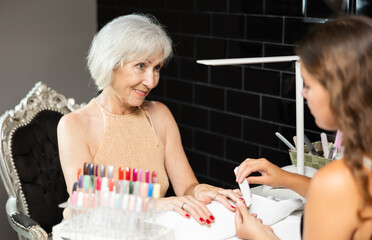 Unrecognizable young woman skilled manicure master carefully files and grooms nails of senior...