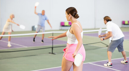 Rear view of young woman in sportswear playing pickleball tennis on court. Racket sport training...