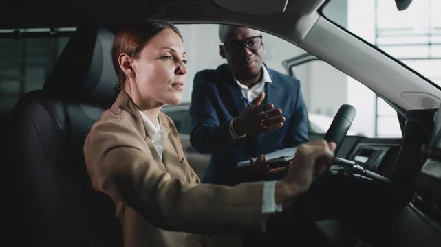 A car dealer consults a young woman in a modern showroom as she prepares for a test drive of a new vehicle. Concept exploring new car experience.