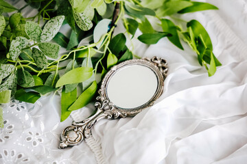 Decorative vintage mirror surrounded by green leaves on a soft white fabric backdrop
