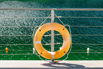 Bright yellow lifebuoy hangs on railing by calm green water during a sunny day