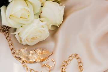 Elegant golden necklace beside white roses on satin fabric in soft lighting