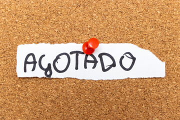 Handwritten word Agotado pinned on a cork board, indicating a sold-out status. Communicates unavailability and serves as a notice for potential customers.