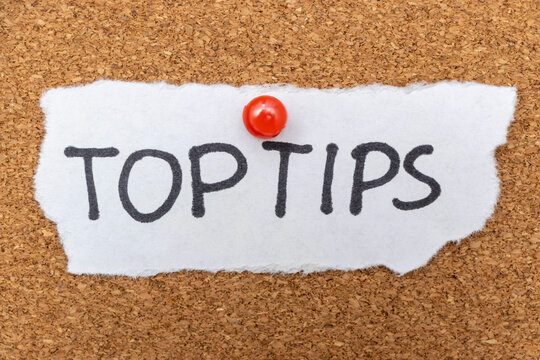 Handwritten note reading top tips pinned on a corkboard. This image conveys advice sharing and can be used in educational or business contexts.