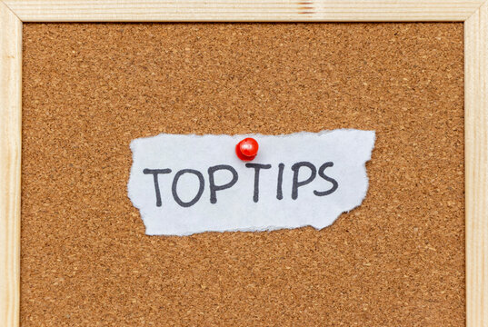 Handwritten note reading TOP TIPS pinned on a corkboard. Useful for advice, motivation, or reminders. Perfect for organization and inspiration in an office space.