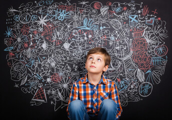 Pensive young boy gazes at complex chalkboard drawings exploring new ideas and creative possibilities at school