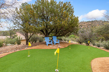 A beautiful putting green featuring blue chairs and a tree in the background