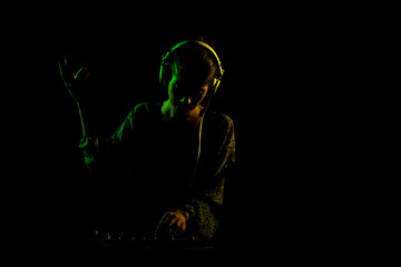 Female DJ with headphones on a mixer. Side lit silhouette of a girl playing techno music against...